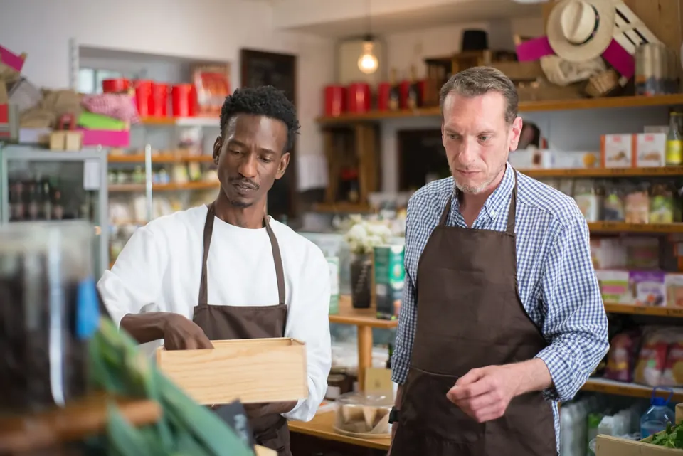 Two shop owners in aprons sorting stock together.